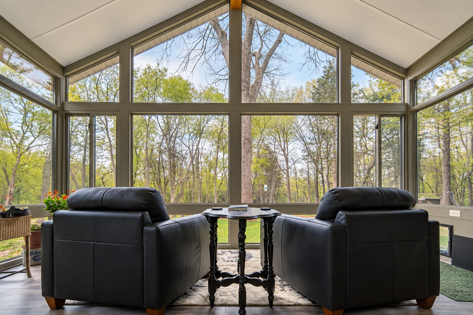 An all-season room with two black leather recliners faces tall windows and a peaked glass ceiling overlooking trees.
