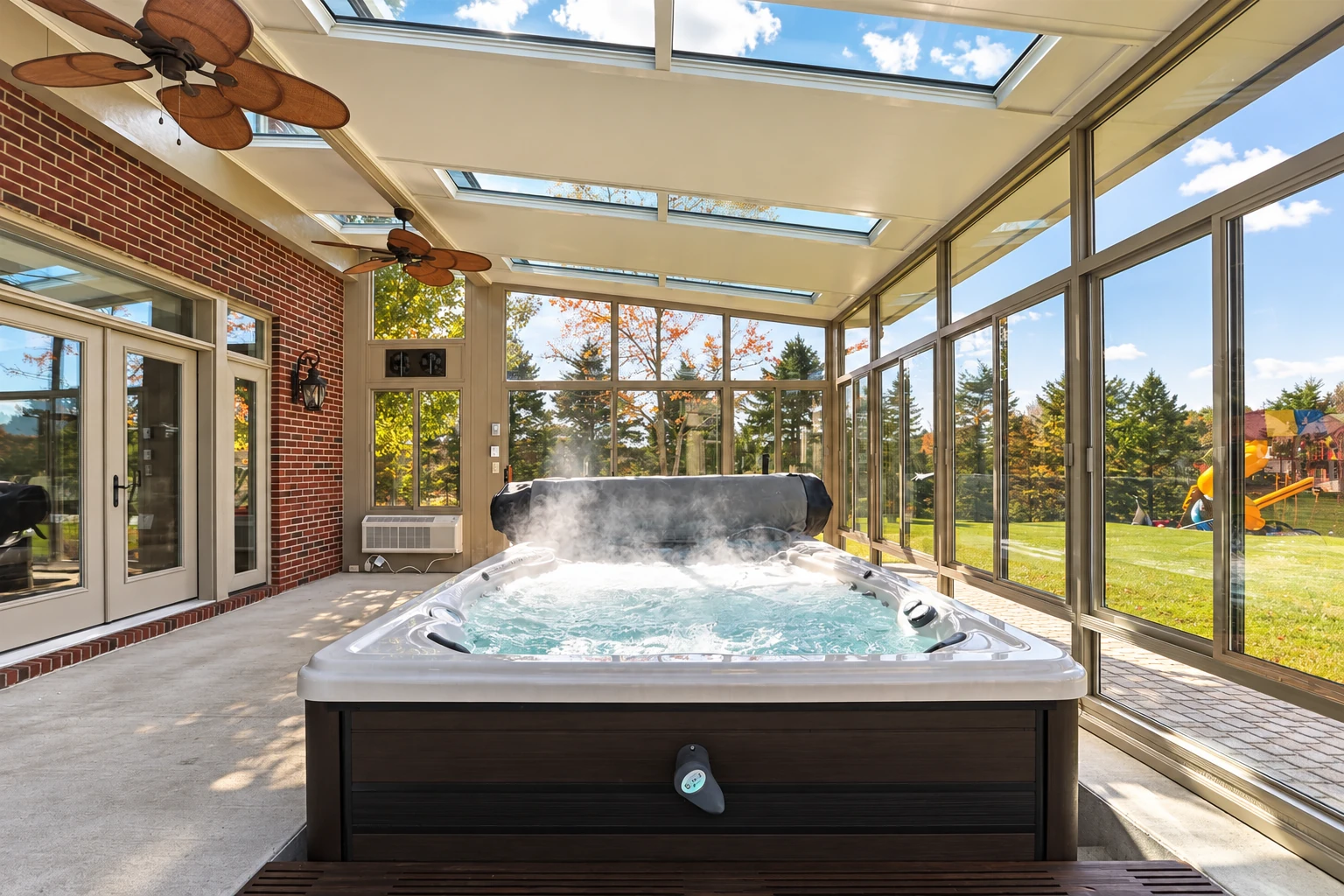 Enclosed patio room with a bubbling hot tub, skylights, ceiling fans, and broad glass walls.