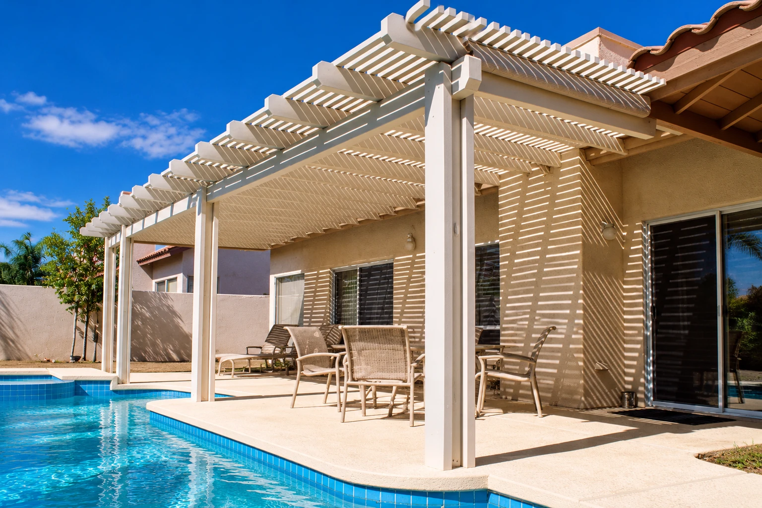 A white slatted patio cover shades outdoor seating beside a swimming pool.