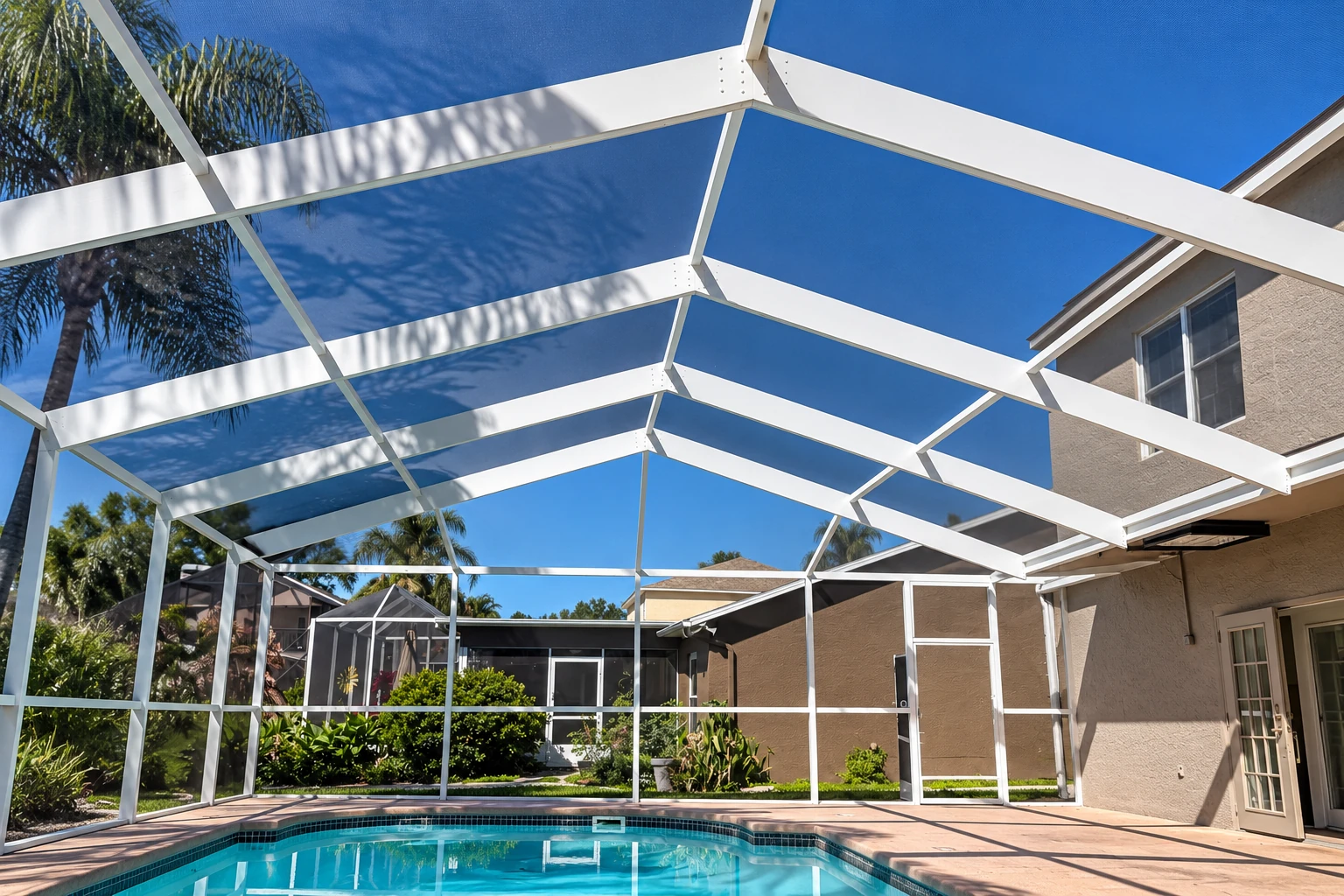 A white-framed screen enclosure covers a backyard swimming pool, with palms and neighboring homes visible beyond the mesh.