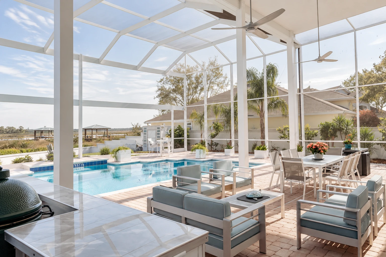 Bright pool patio enclosure with a white-framed glass roof, ceiling fans, lounge seating and dining table.
